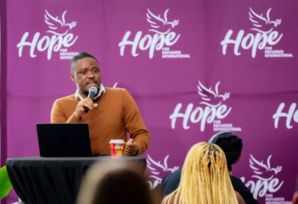 Patrick King Mwesigye, Founder and Director of Programs at Hope for Refugees International giving welcoming remarks at the symposium.